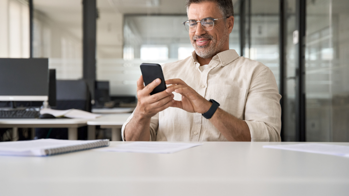 Un hombre con gafas usando su teléfono celular en su oficina