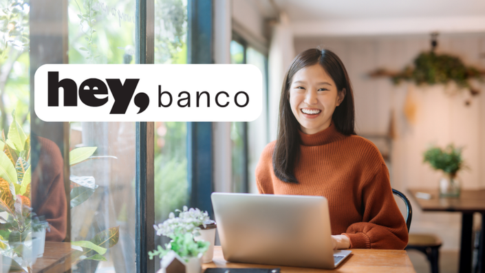 Una persona sonriente trabajando en su laptop en un espacio luminoso, aprovechando los servicios de hey, banco