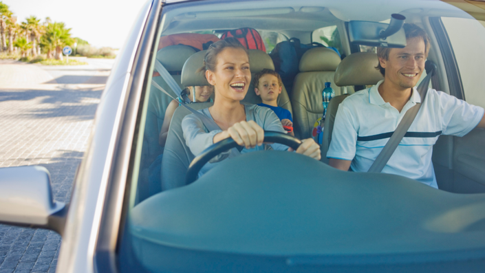 Una familia feliz dentro de un auto mientras revisan una aplicación móvil de seguros.