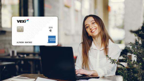 Una mujer sonríe mientras usa su laptop en un ambiente moderno, con la tarjeta de crédito Vexi (American Express) visible sobre la mesa.