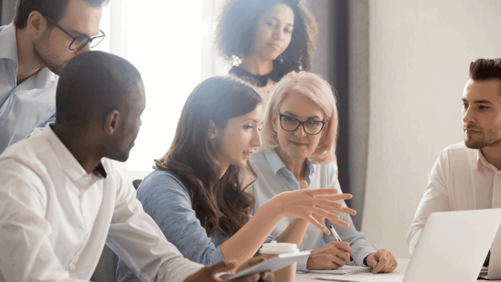 Un grupo diverso de profesionales en una reunión de oficina, donde una mentora asesora a un equipo sobre una estrategia para invertir en startups. La escena transmite colaboración y planificación.