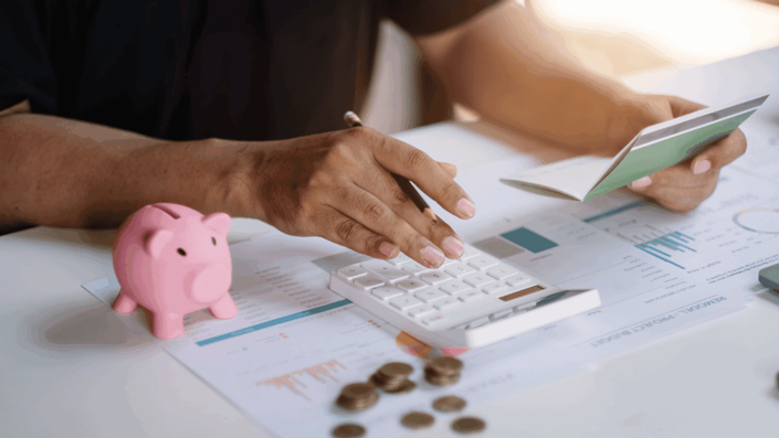 Persona revisando un presupuesto o plan financiero con una alcancía rosa y monedas, representando el proceso de planificación para alcanzar la libertad financiera.