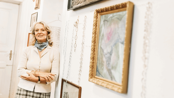 Mujer coleccionista de arte posando junto a una pintura enmarcada en su galería personal, simbolizando la confianza y el conocimiento necesarios para invertir en arte.