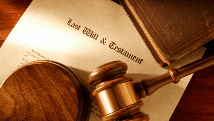 Un documento antiguo con el título 'Last Will & Testament' (Última Voluntad y Testamento) en una mesa de madera, junto a un mazo de juez y un libro encuadernado en cuero, simbolizando la formalidad y la importancia legal de hacer un testamento.