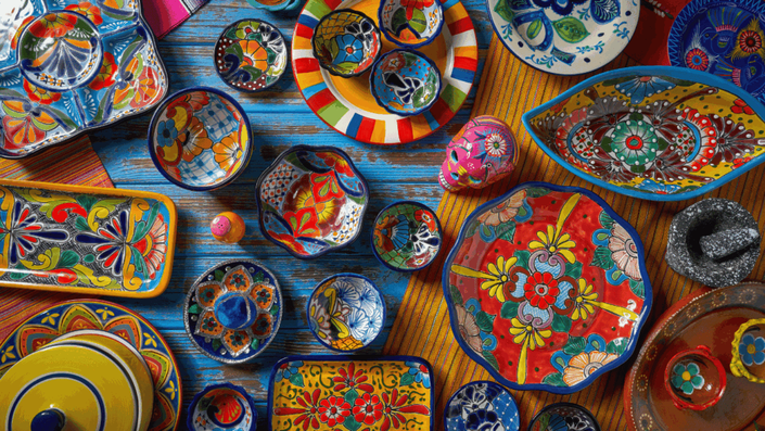Colección diversa de cerámica y arte popular mexicano, con platos y tazones coloridos sobre una mesa, mostrando la riqueza cultural y el atractivo de invertir en arte.