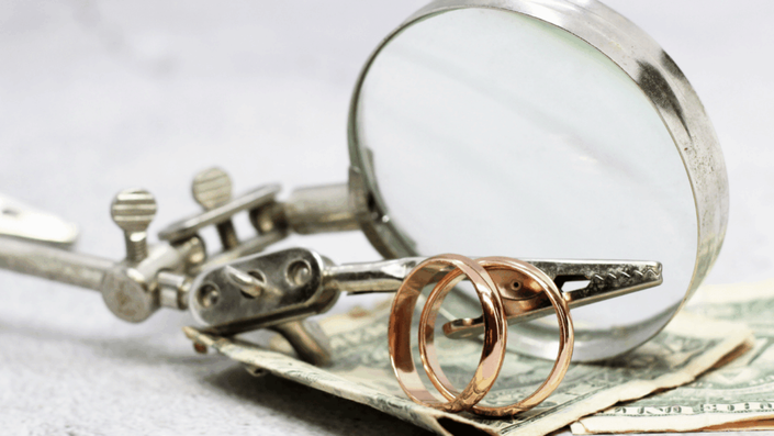 Anillos de oro frente a una lupa sobre billetes de dólar, representando la evaluación y el empeñar oro para obtener el mejor precio.
