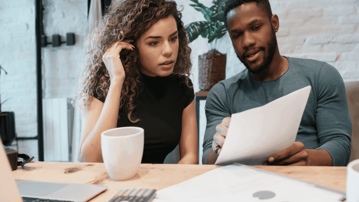 Una pareja en una mesa con una taza de café y una laptop, representando la discusión y planificación de las finanzas en pareja.