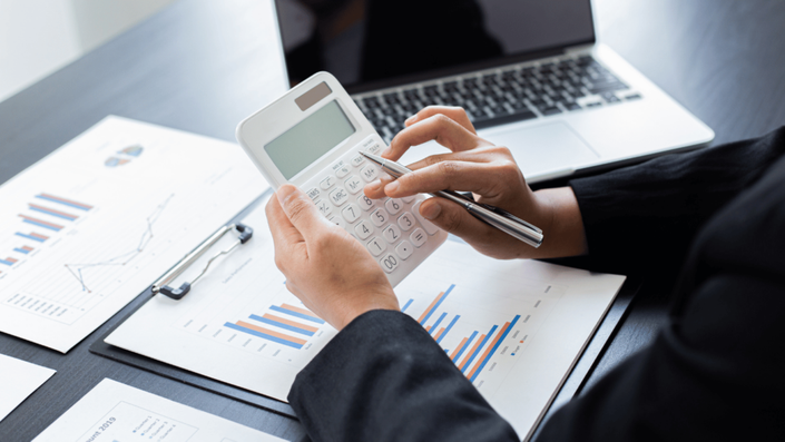 Persona revisando gráficos financieros y utilizando una calculadora para organizar su presupuesto personal.