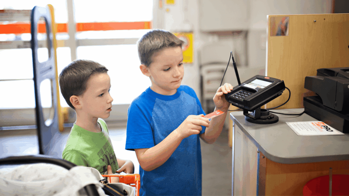 Niños aprendiendo a usar una tarjeta de crédito en un proceso de pago, lo que puede ser una lección importante sobre el manejo responsable del dinero en el contexto del presupuesto familiar.