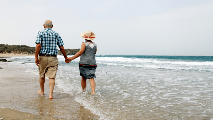 Pareja de jubilados caminando por la playa, disfrutando de su retiro gracias al sistema de pensiones y el ahorro a largo plazo.
