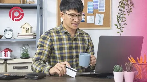 el hombre mira felizmente la pantalla del portátil sosteniendo una taza y una tarjeta de crédito