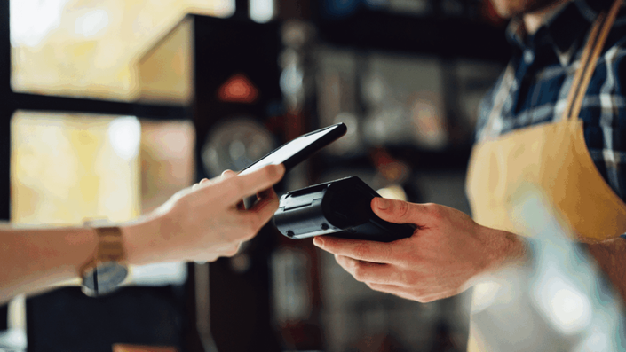 Un cliente acerca su celular a una terminal para pagar, mostrando la facilidad de uso de las tarjetas de crédito virtuales en México en un comercio.